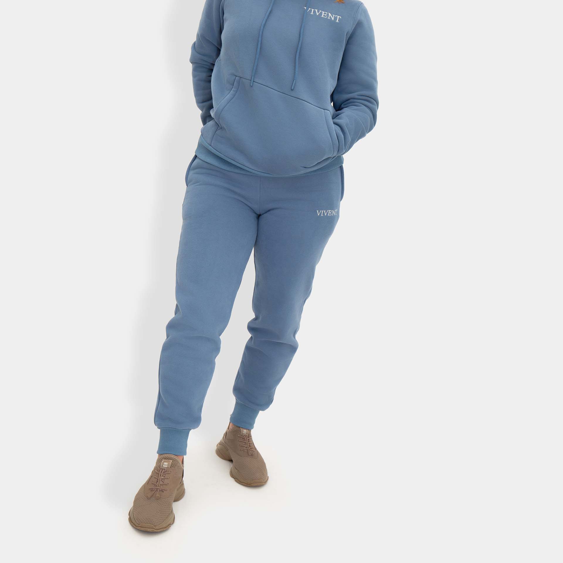 A woman in a blue vivent hoodie and sweatpants, looking casual and comfortable.