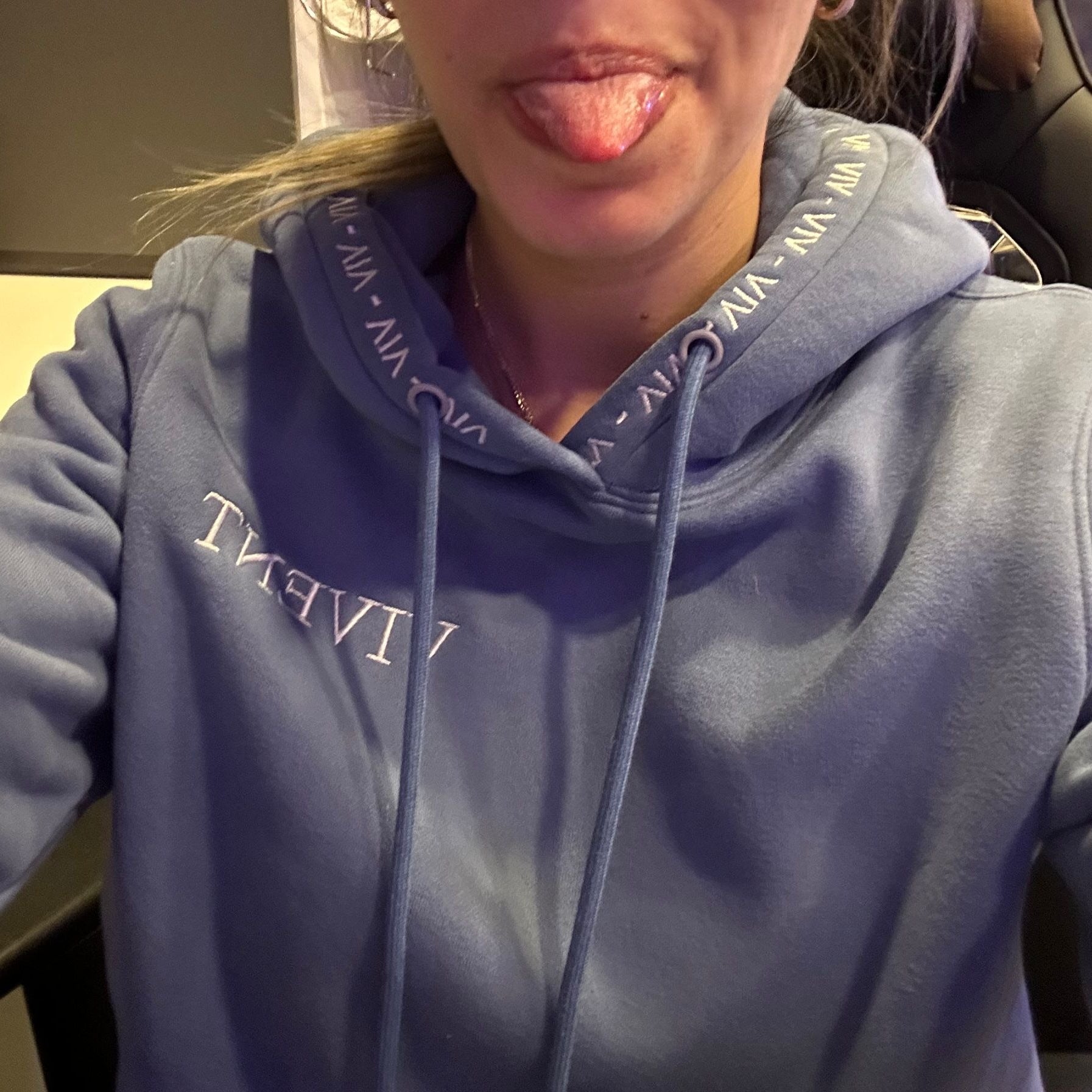 A woman in a blue vivent hoodie playfully sticking her tongue out.