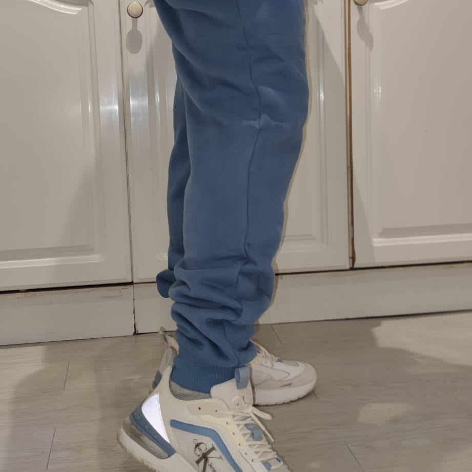 A person in blue vivent sweatpants standing at a kitchen counter.