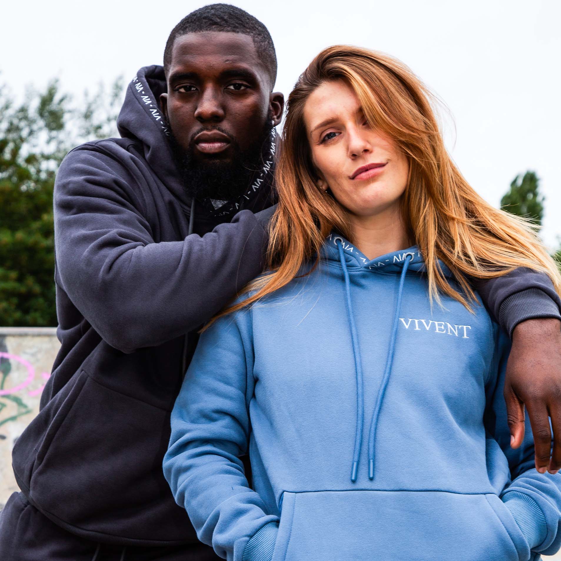 A couple wearing vivent hoodies, standing side by side. They appear relaxed and casual, with their hoods up.